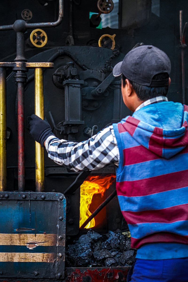 A man managing the controls of a coal-powered steam locomotive, enhancing its classic engineering.