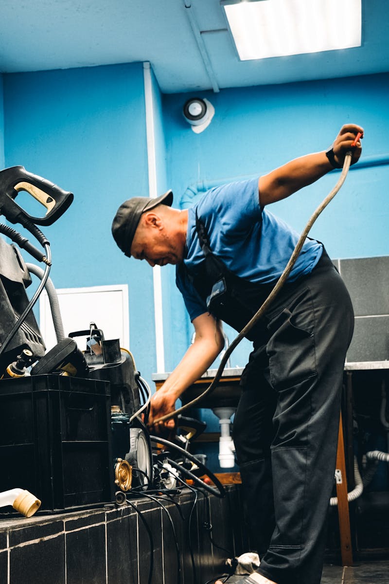 A technician in blue attire repairing equipment in an indoor workshop setting.