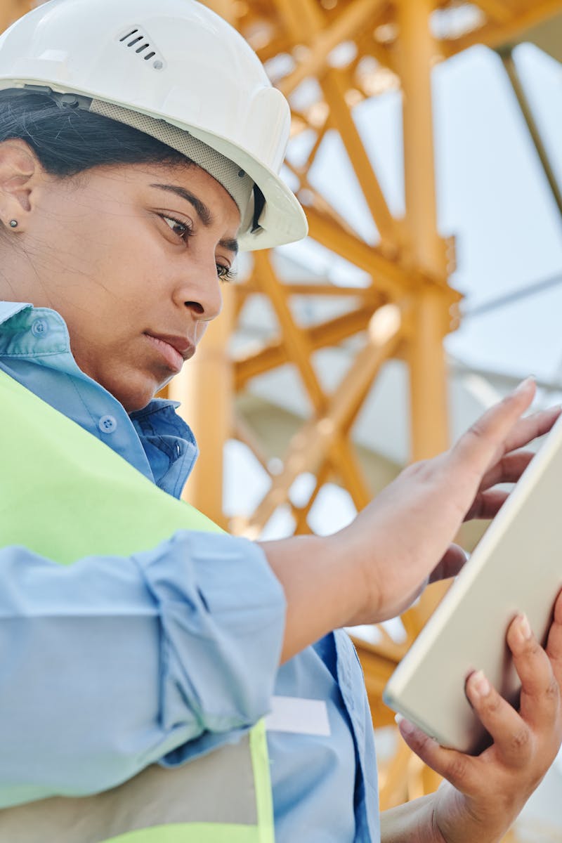A female engineer in workwear checks her tablet on a construction site, highlighting modern engineering practices.